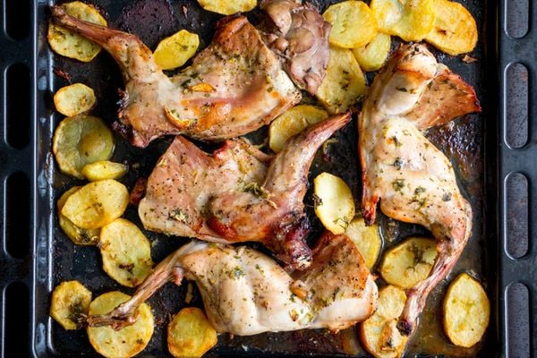 Roasted rabbit with potatoes and herbs on a oven tray. Top view