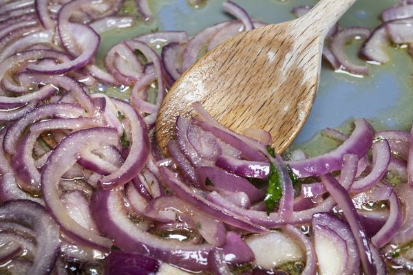 Stirring sauteing red onions with wooden spoon in cooking pan, closeup