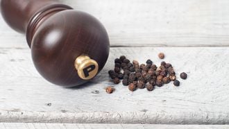 Pepper mill and black peppercorn against wooden table