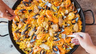 Mixed paella and hands with forks taking rice. Aerial view.