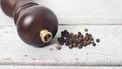Pepper mill and black peppercorn against wooden table