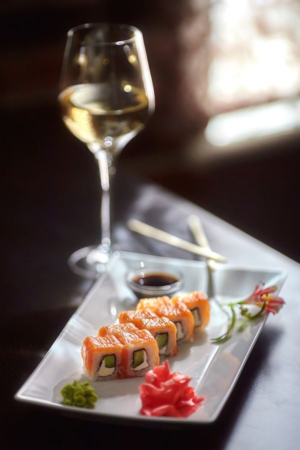 Philadelphia maki sushi rolls with salmon, cheese cream, cucumber on white plate and glass of wine