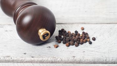 Pepper mill and black peppercorn against wooden table