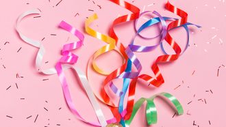 Flat lay of Celebration. Champagne bottle with colorful party streamers on pink background.